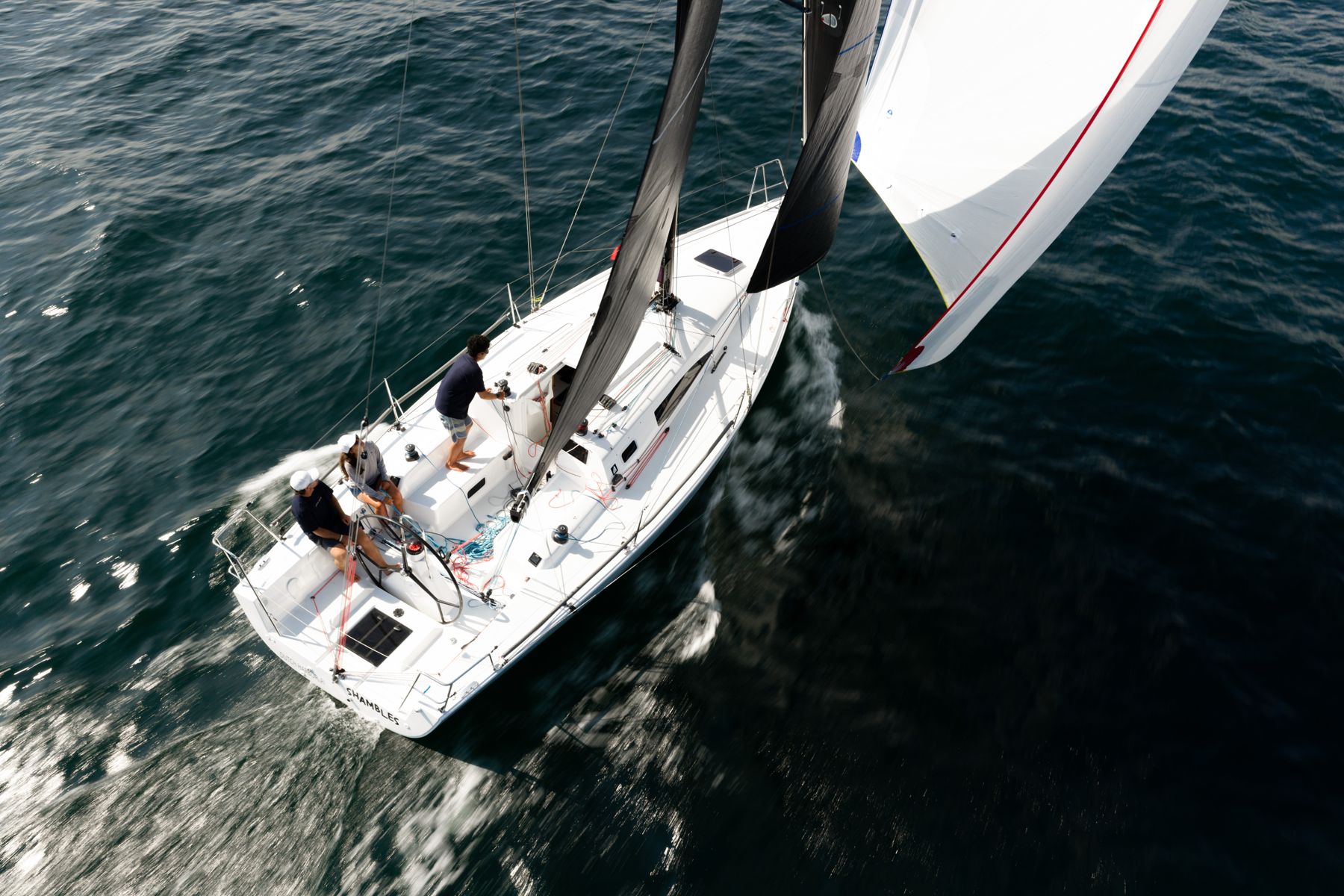 Aerial view of a J/Boat sailing fast under main and gennaker, crew in the cockpit