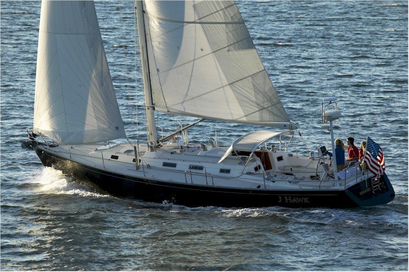 The cruising J/Boat J Hawk sailing under main and genoa with family aboard and an American flag on the stern